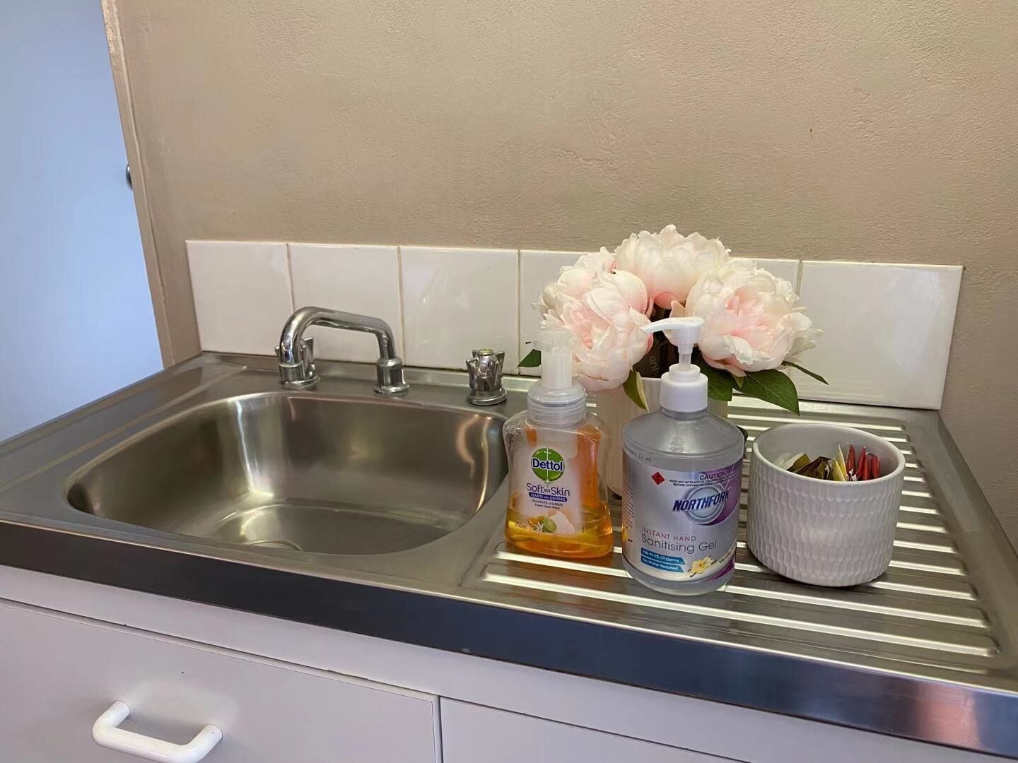 A kitchen sink with a faucet, a bottle of Dettol Soften Skin hand wash, a bottle of Northfork Instant Hand Sanitising Gel, and a cup with utensils.