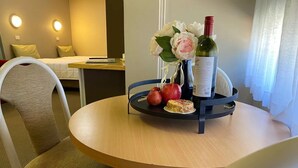 A hotel room with a round wooden table, a vase with flowers, a bottle of wine, and a plate with fruits and a cake. - Apollo Motel Parkes (Parkes)