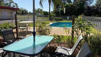 An outdoor patio area with a pool, surrounded by a fence and greenery.