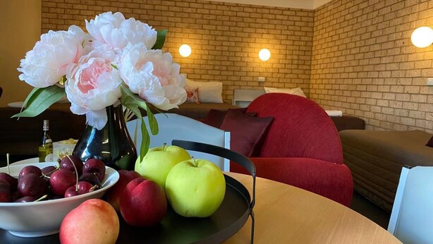 A modern living room with a brick wall, a red sofa, and a wooden table with fruits and flowers. - Apollo Motel Parkes (Parkes)