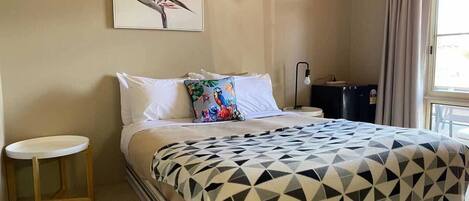 A hotel room with a bed, a small bedside table, a lamp, and a window with curtains.