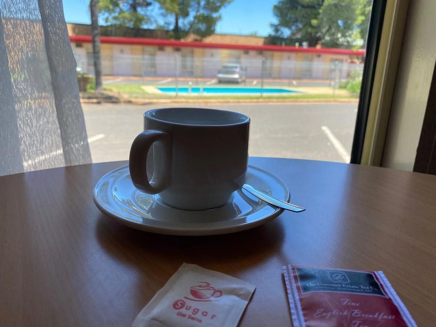 Une tasse de café posée sur une soucoupe, avec une cuillère sur la table, un sachet de sucre et un menu également sur la table.