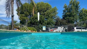 A swimming pool with clear blue water, surrounded by a fenced area with trees and a white vehicle parked nearby. - Apollo Motel Parkes (Parkes)