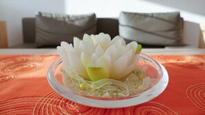 Un cuenco de vidrio transparente con un arreglo de flores de loto blancas sobre un mantel naranja estampado.