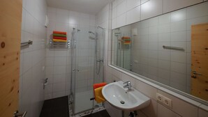 Un baño con cabina de ducha de vidrio, un lavamanos blanco y un espejo grande.