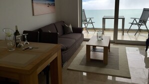A living room with a sofa, a coffee table, and a glass of wine on a wooden table. There is a painting of a beach on the wall, and a view of the sea through the glass door. - Private hillside location ★★★★ with special views, ideal for couples (Medveja)