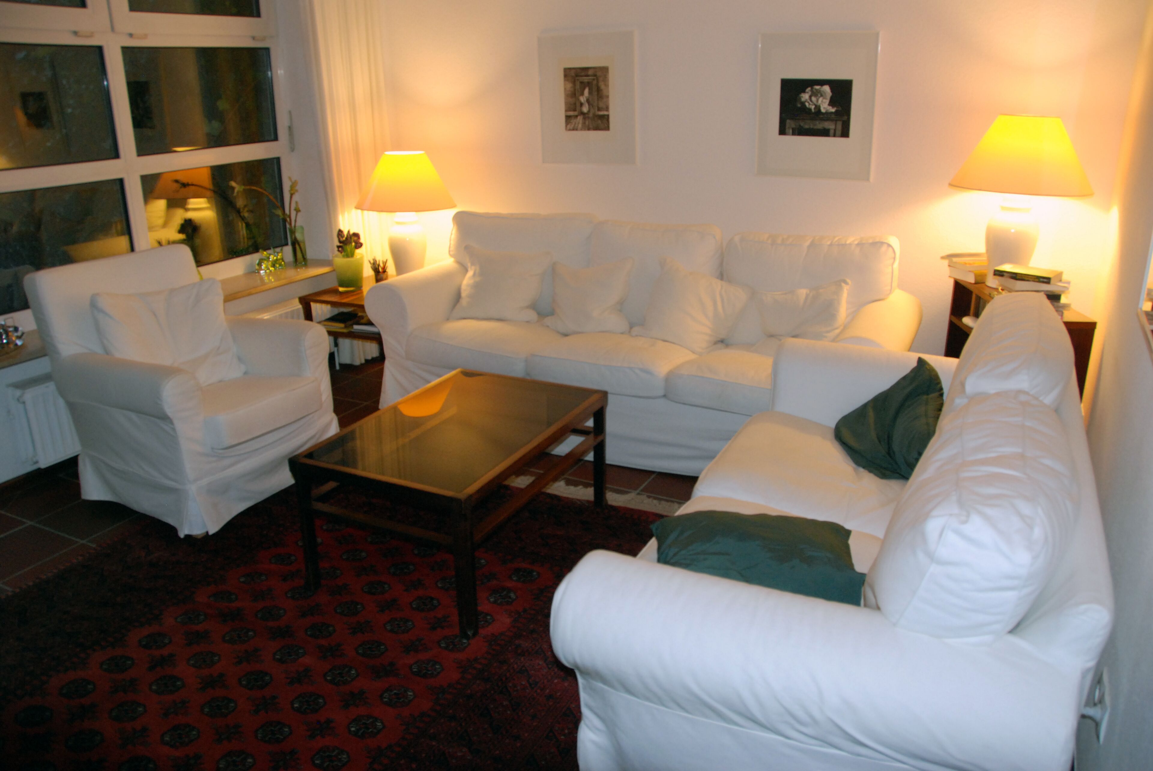A living room with a white sofa, a white armchair, a glass coffee table, and two lamps on side tables.