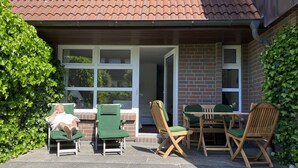 Een terras met buitenmeubilair, waaronder stoelen en een tafel, en een persoon die in een stoel ligt.