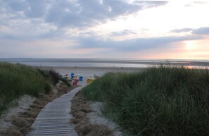 A wooden boardwalk leading to a beach with sand and grass on either side. - Langeoog: Cozy vacation home with sun terrace (Langeoog)