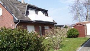 A two-story house with a sloped roof, a visible chimney, and a small attached garage. - Peaceful well furnished apartment near the North Sea spa Büsum (Westerdeichstrich)