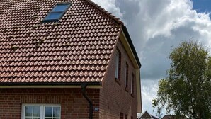 A red brick building with a tiled roof, a paved driveway, and a small red structure in the background.