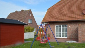 A residential area with a swing set in a backyard, a red wooden shed, and a brick house with a tiled roof.