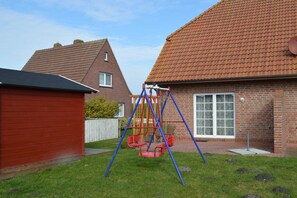 Asuinalue, jossa on leikkipuisto takapihalla, punainen puinen varasto ja tiilitalo, jonka katto on päällystetty tiilillä.