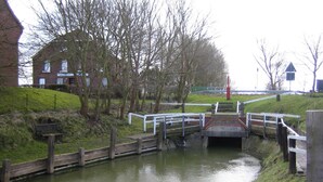 A canal with a small bridge, a bench, and a building in the background.