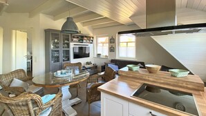 Een moderne keuken met witte kasten, een houten aanrechtblad en een eethoek met rieten stoelen en een glazen tafel.