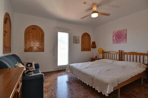 A bedroom with a bed, a desk, a chair, a ceiling fan, and wooden cabinets.