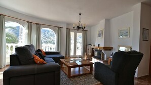 A living room with a sofa, armchair, coffee table, fireplace, and large windows with curtains. - Peaceful Villa with heavenly sea view and panoramic view (Calp)