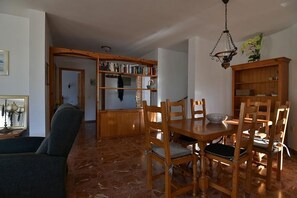 A dining area with a wooden table and chairs, a bookshelf, and a chandelier.