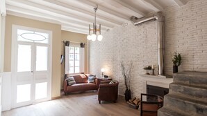 A living room with a brown leather sofa, a coffee table, and a fireplace. There is a brick wall and a wooden ceiling.