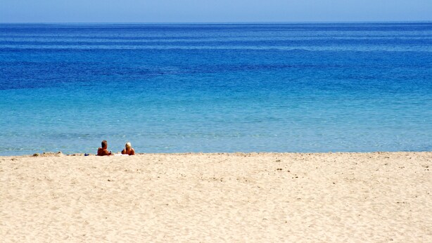 A beach with clear blue water and a sandy shore.