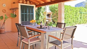 An outdoor patio with a wooden table and chairs, a potted plant, and a grill.