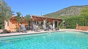 A pool area with lounge chairs and a building with a tiled roof.