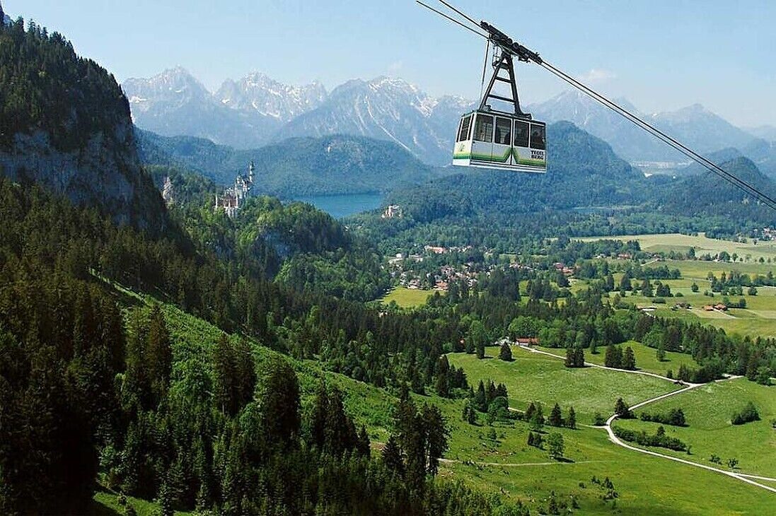 A cable car moving over a mountainous landscape with a castle-like structure in the distance.