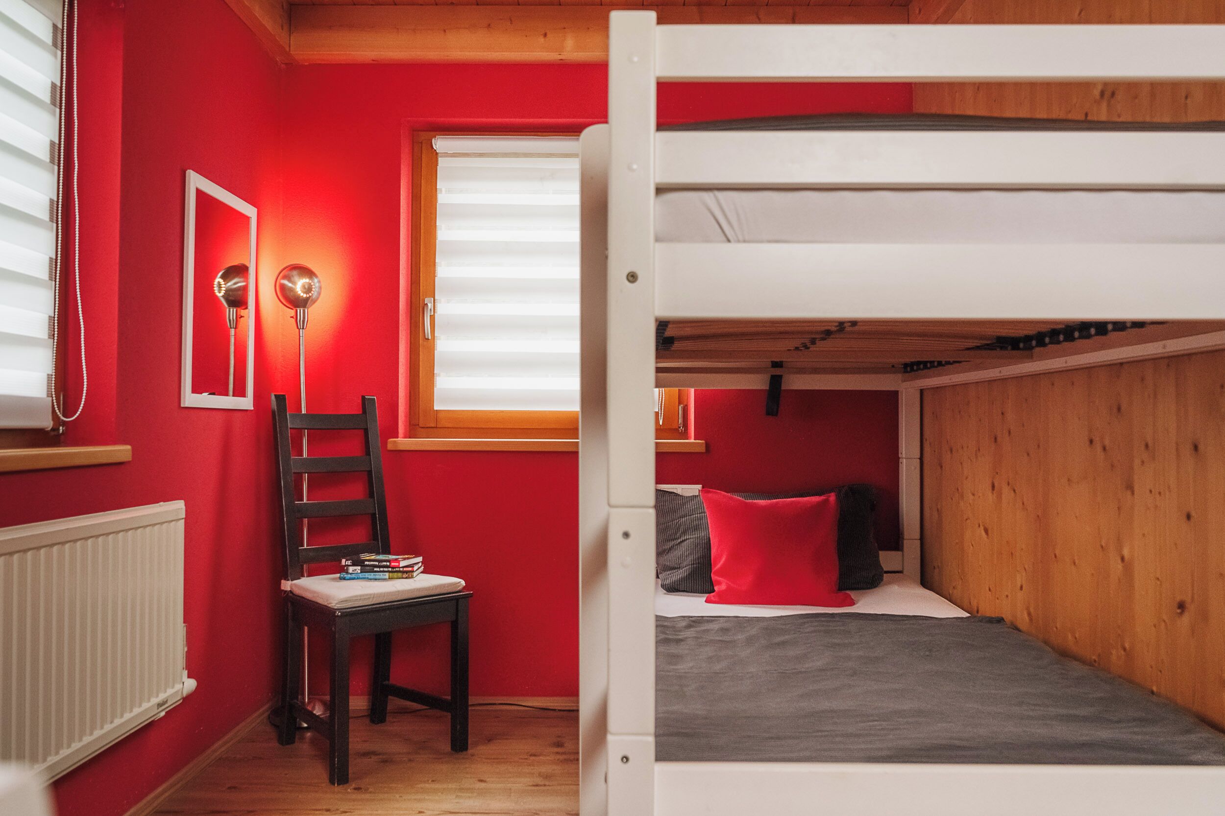 Una habitación con una cama litera, un escritorio con silla, un espejo y un radiador.