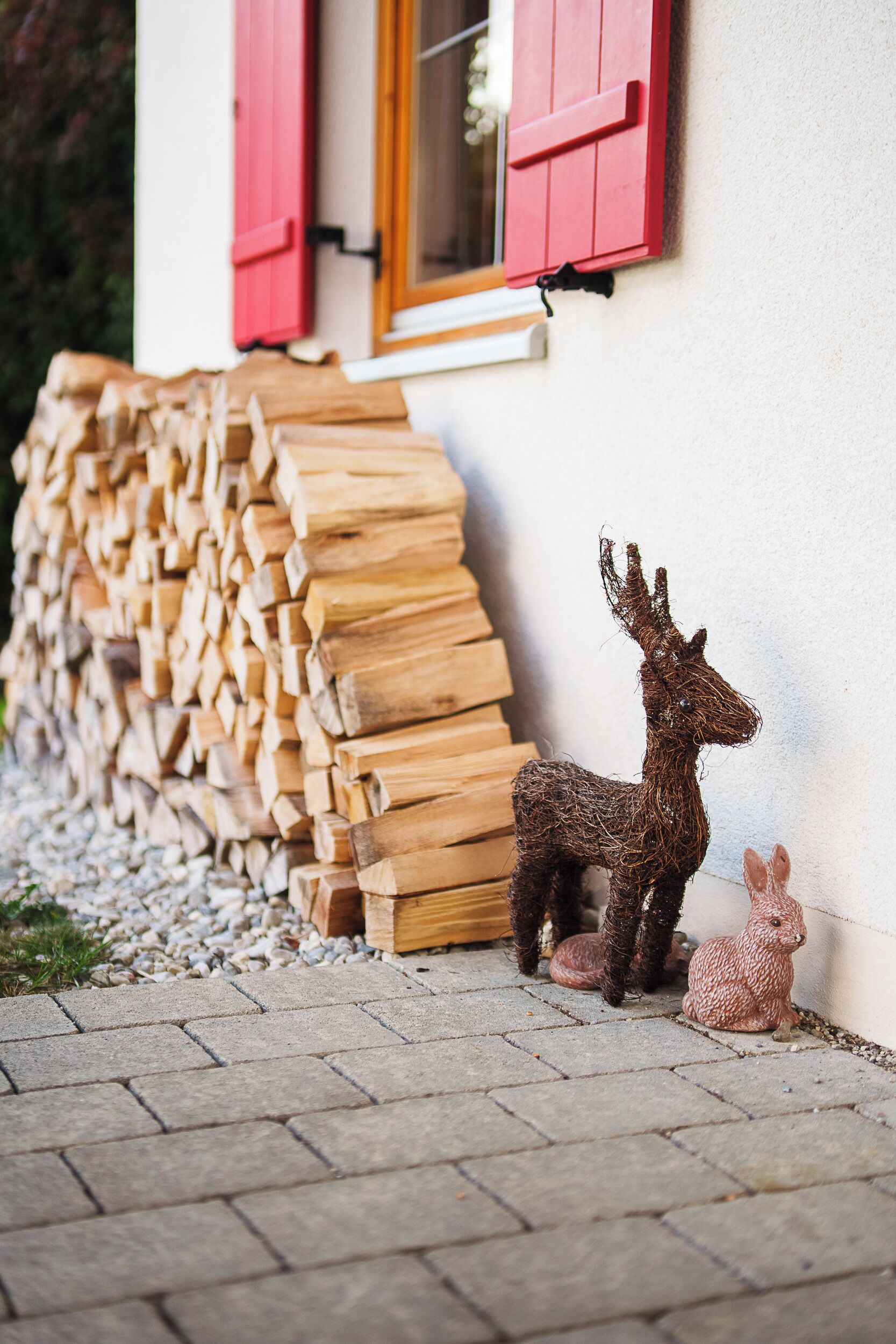 A stack of firewood against a building with red shutters and a small deer figurine beside it.