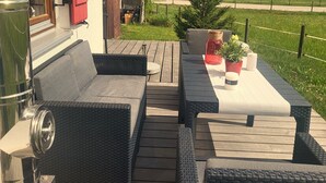 Una terraza de madera con muebles de mimbre, una parrilla y plantas en macetas.