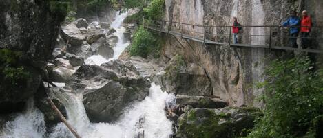 Un pont suspendu surplombant une cascade, avec un terrain rocheux et une végétation luxuriante.
