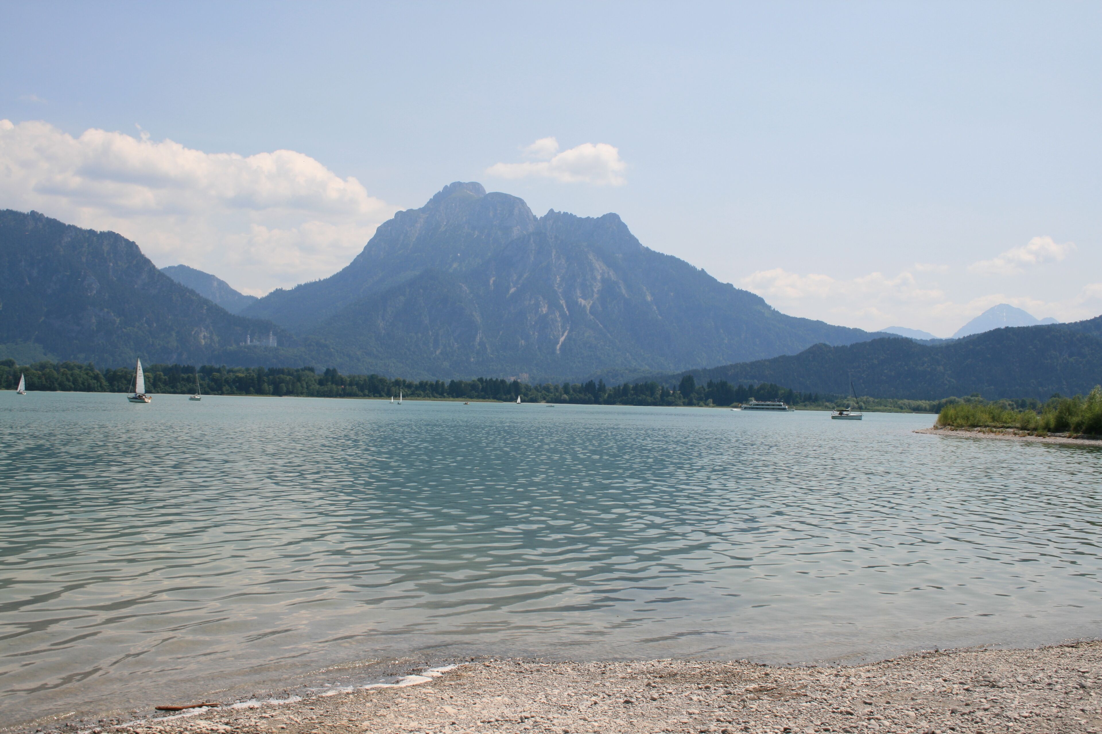 A calm lake with sailboats and mountains in the background.