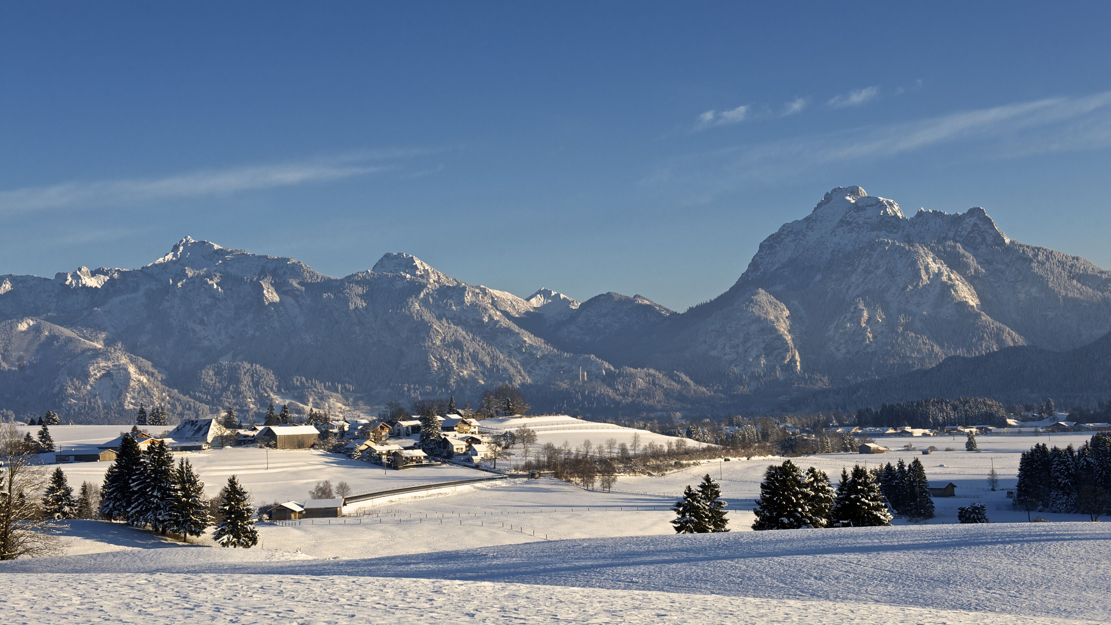 A snow-covered landscape with mountains in the background and a few buildings in the foreground.