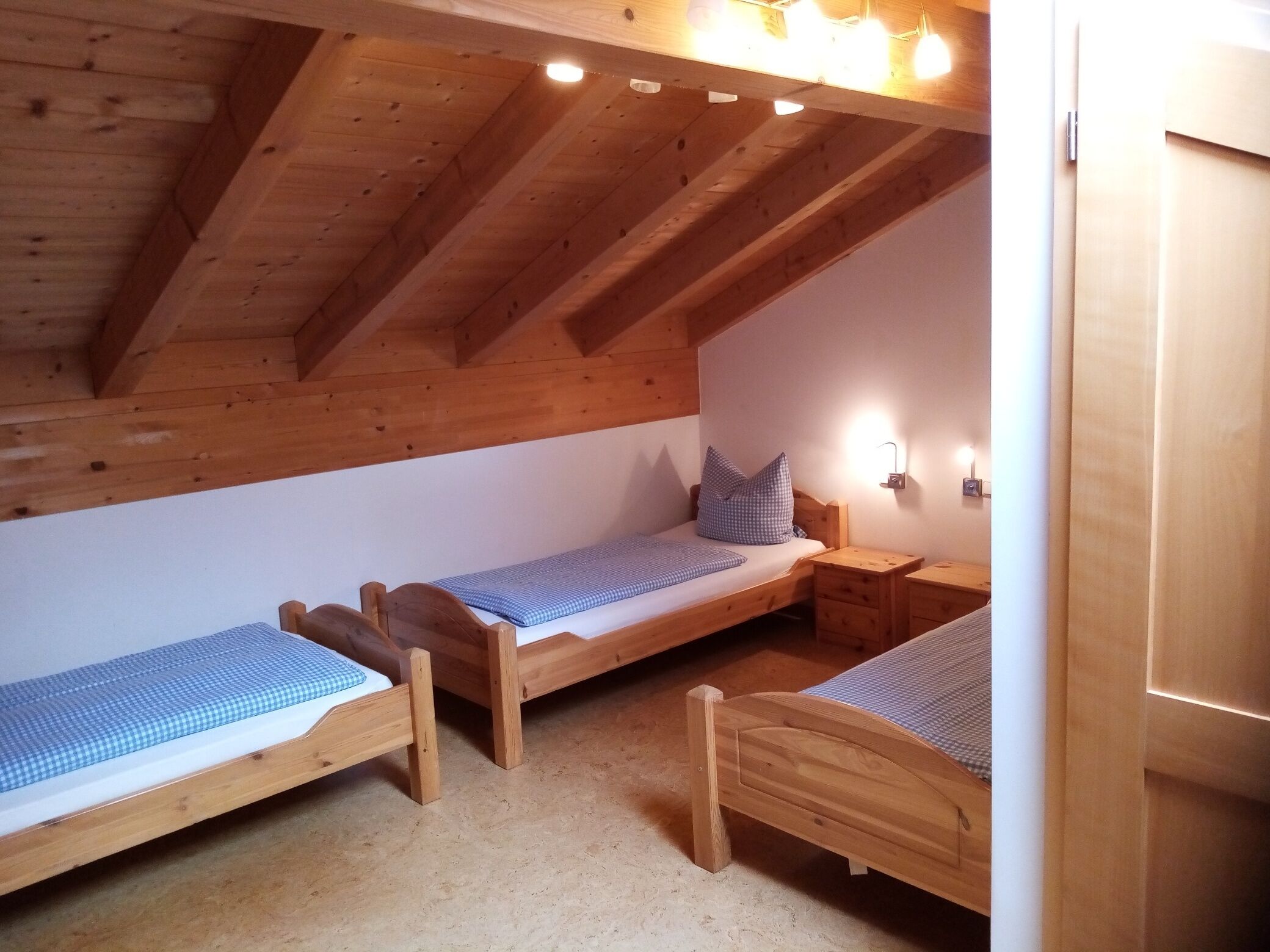 Una habitación pequeña y acogedora con dos literas de madera, techo de madera y una lámpara fijada a la pared.