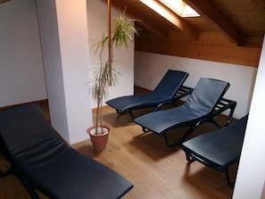 Une pièce avec des poutres apparentes en bois au plafond, une plante en pot et trois fauteuils noirs.