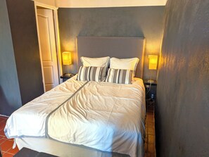 A bed with a headboard, two bedside lamps, and a bedside table with a book and a lamp.