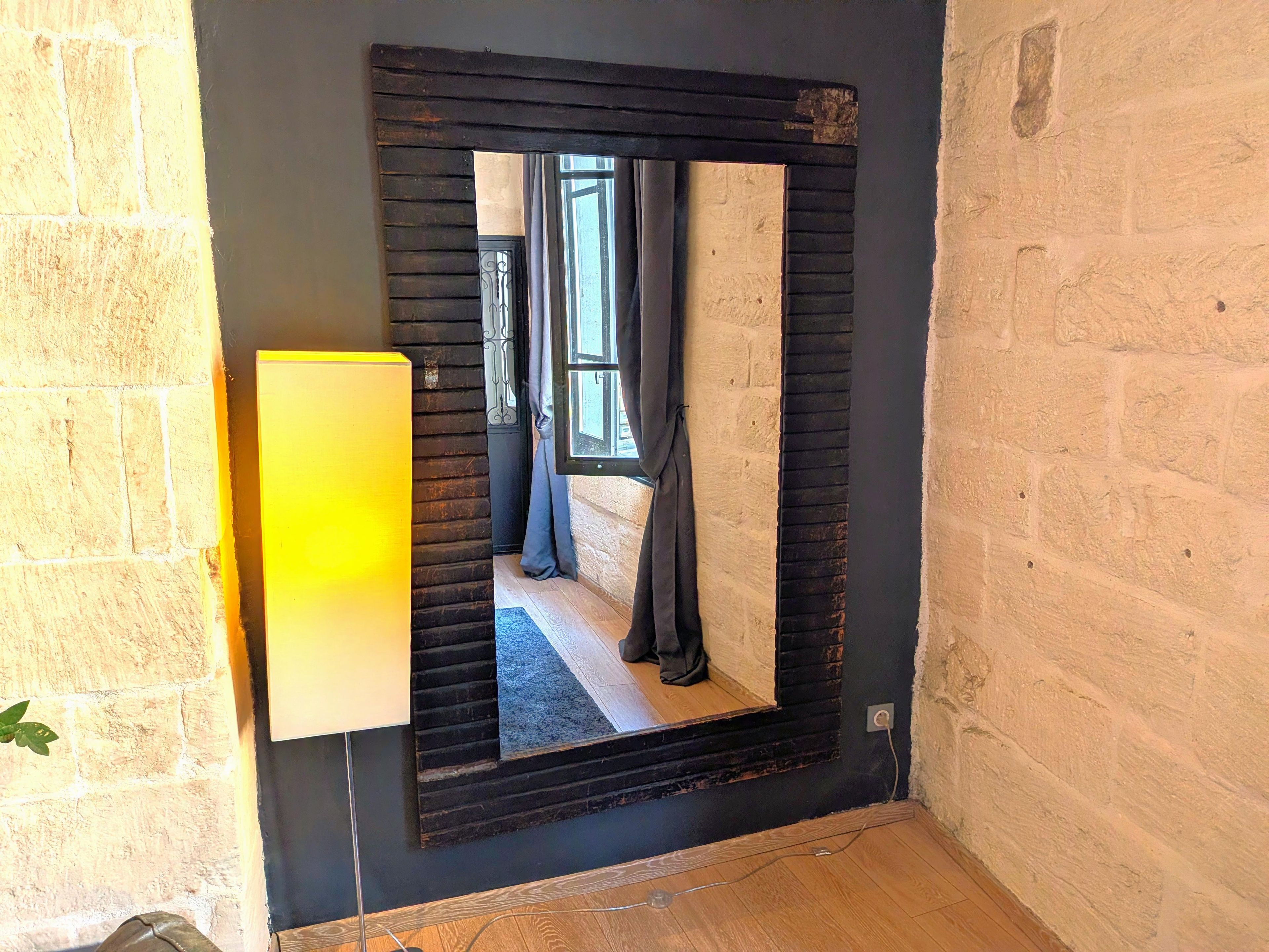 A mirror with a black frame mounted on a wall with a brick pattern.