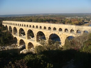 A long stone aqueduct with multiple arches spanning a valley, surrounded by trees and distant buildings.