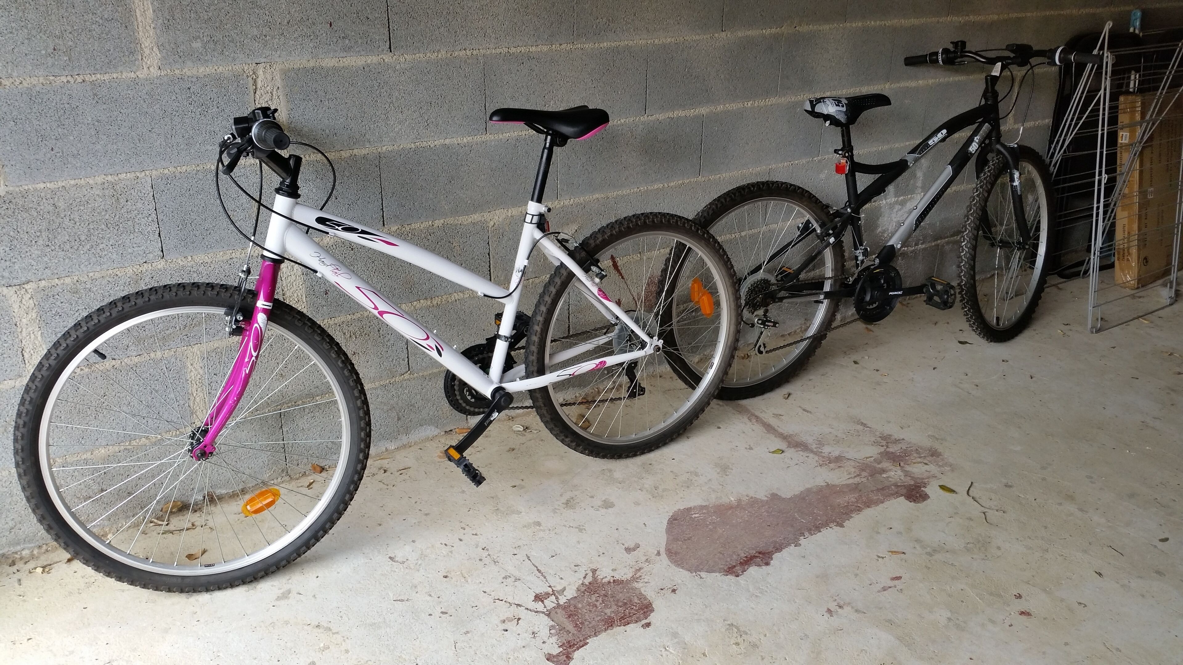 A white bicycle with pink accents parked against a concrete wall in a covered area.