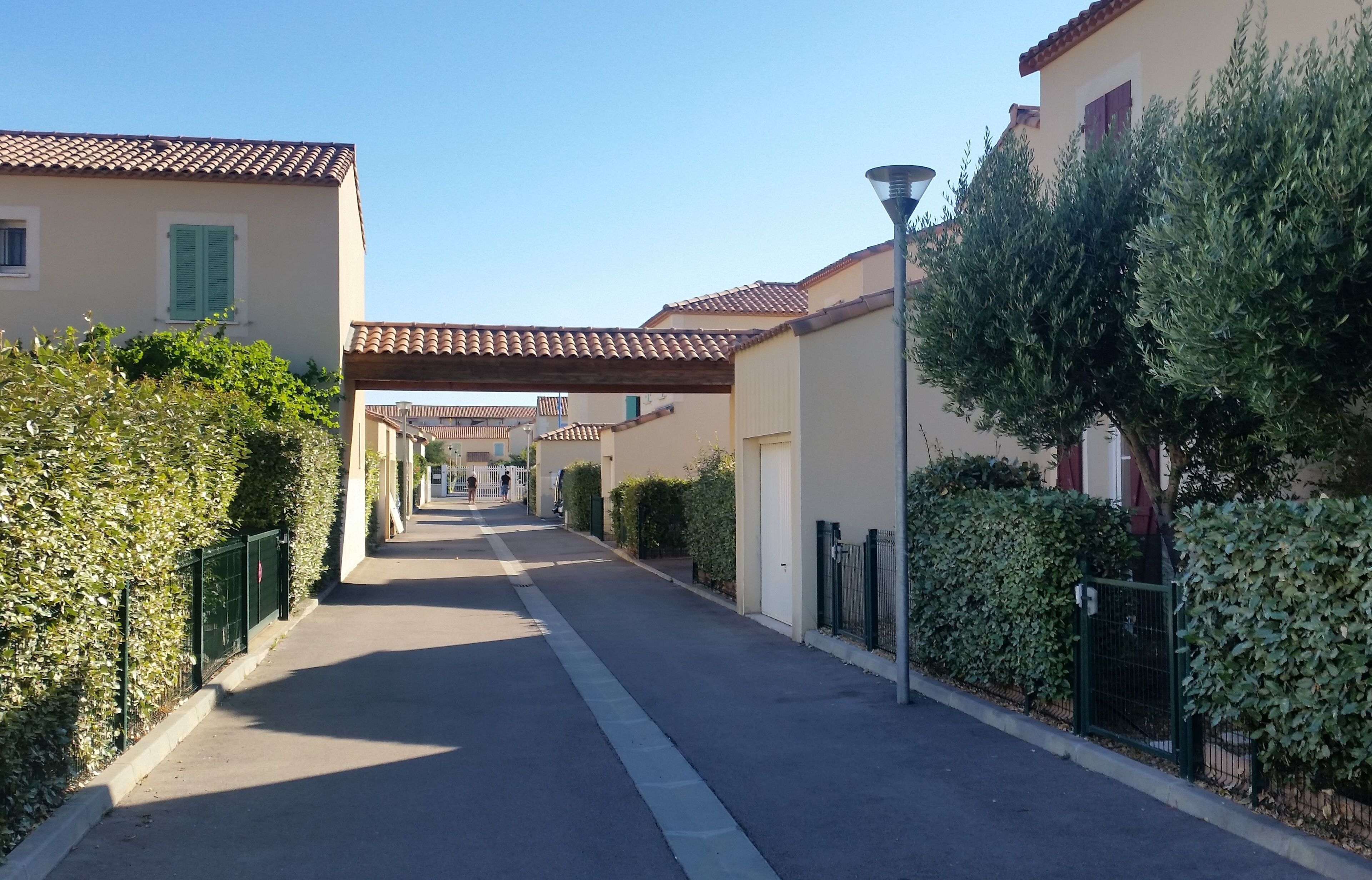 Una calle estrecha flanqueada por edificios, cielo despejado y una senda peatonal.