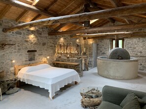 A rustic room with a stone wall, wooden beams, a bed, a stone fireplace, and a green sofa.