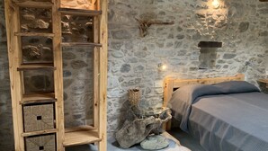 Una stanza rustica con parete in pietra, mensole di legno, un letto con testiera e una scultura in pietra.