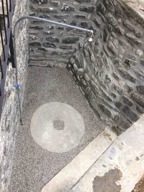 A stone-walled room with a circular stone floor, a metal railing, and a small window.