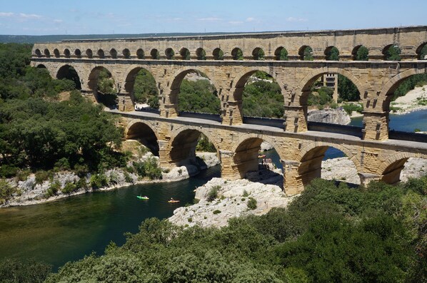Un puente de acueducto de piedra sobre un río, con múltiples arcos, rodeado de vegetación y terreno rocoso.