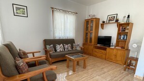 A living room with a sofa, armchair, coffee table, wooden cabinet, TV stand, and a fan. - Small house in a village, with a front yard, set back from the main street, with Wi-Fi (Valle Gran Rey)