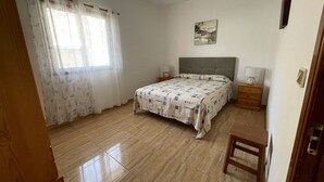 A bedroom with a bed, two bedside tables, a nightstand, a window with curtains, and a wall-mounted picture. - Small house in a village, with a front yard, set back from the main street, with Wi-Fi (Valle Gran Rey)