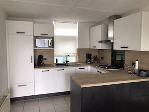Een moderne keuken met witte kasten, een zwart aanrecht, een ingebouwde magnetron, een gasfornuis en een raam met zonwering.