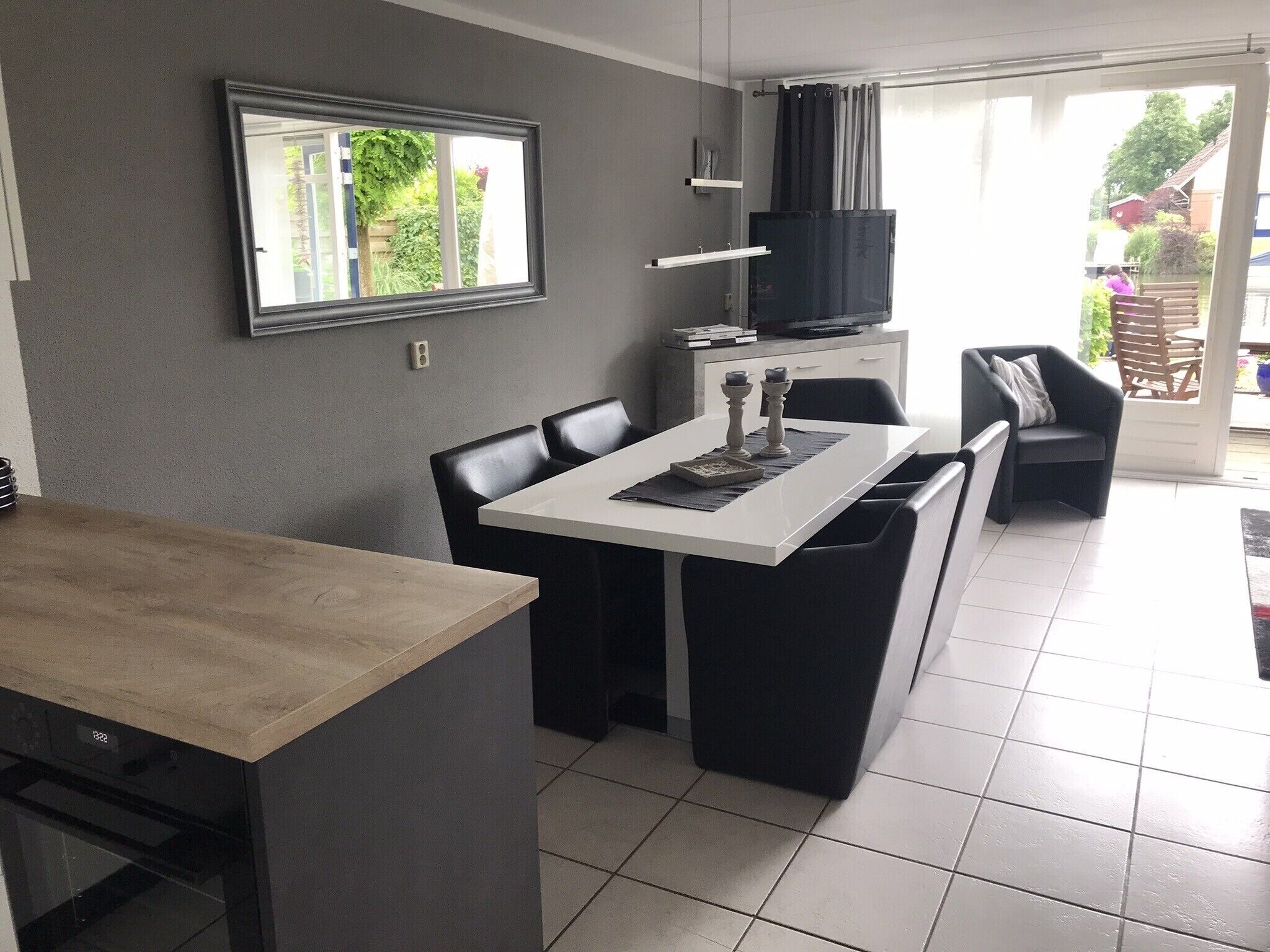 A modern kitchen with a dining area, featuring a large window, a built-in oven, and a flat-screen TV.