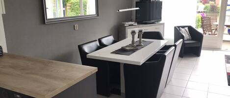 A modern kitchen with a dining area, featuring a large window, a built-in oven, and a flat-screen TV.