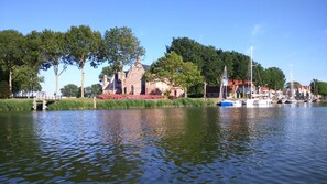 Um edifício histórico com um fosso, rodeado por árvores e barcos na água.